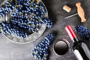 Red wine bottle and full glass, grapes on dark stone table top view. Vine concept on black...