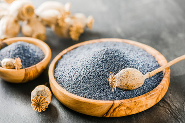 Poppy seeds in wooden bowl side view. Poppies dried heads on dark stone table.