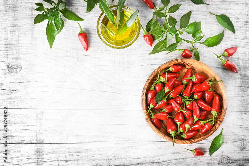 Wall mural Hot spicy peppers in wooden bowl on white rustic table. Chili pepper top view copy space.