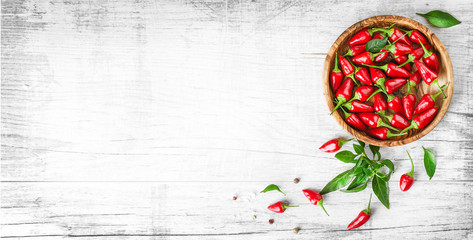 Red fresh chili peppers in wooden bowl on white old table. Spicy or hot small pepper with green...