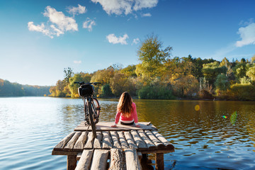 girl sits on the bank of the river. bike on the river with a bag on the trunk