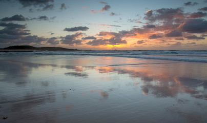 Mirrored coastal reflections in wet beach sand at sunrise