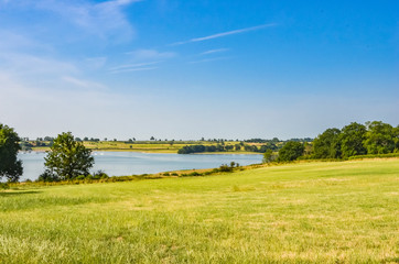 View across Rutland Water a large reservoir in Leicestershire with blue sky and grass.
