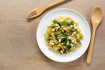 top view of stir fried pickled mustard green with egg in a ceramic dish on wooden table. asian homemade style food concept.