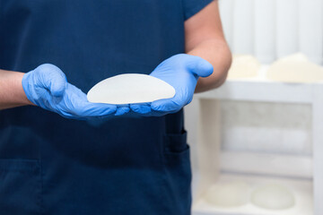 Doctor holding silicone implant for breast augmentation, space for text. Plastic surgeon hands...