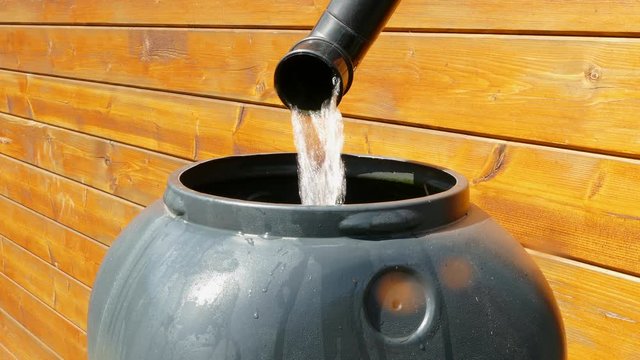 Closeup POV shot of rainwater flowing through the plastic downpipe from the guttering of a wood cabin, into a plastic water butt.