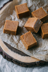 Fresh caramel fudge candies on a wooden plate with copy space in marble background