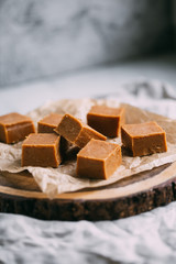 Fresh caramel fudge candies on a wooden plate with copy space in marble background
