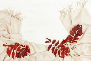 Autumn flat lay with rowan leaves red color and rowanberries on soft autumnal female scarf on white wooden background with copy space. Top view.