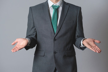 Businessman is spreading his hand aside on gray background. Have no idea.