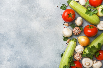 Set of different seasonal vegetables on a gray concrete background. Tomato zucchini onion garlic mushrooms parsley spices. Frame copy space.