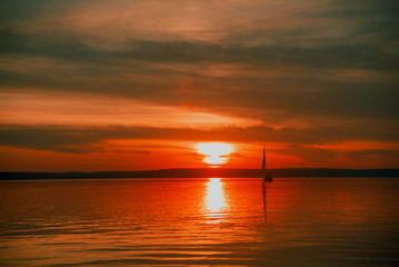 Sailing boat floats on the lake at sunset.