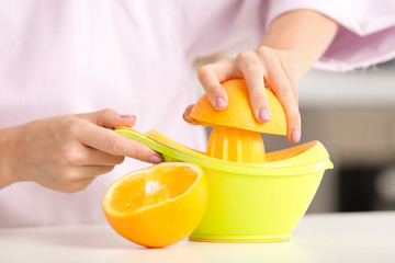 Beautiful young woman making fresh orange juice in kitchen, closeup