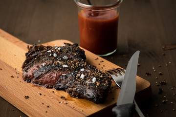 Rinder Hüftsteak auf Holzbrett mit Ketchup, Salz und Steakpfeffer auf Holz Hintergrund dunkel