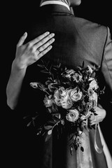Wife hugs her husband holding a wedding bouquet of roses in hand in black and white