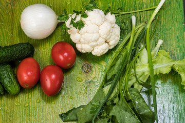 fresh vegetables with drops of water on a green wooden surface, poidor, cucumber, bell pepper, onion, greens, cauliflower