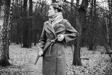 Young attractive woman ties a belt on a coat in autumn park