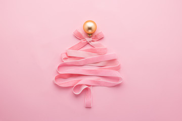 Christmas creative tree made of ribbon decorated with golden ball a pastel pink background. Festive minimalism concept.