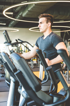 The athletic man dressed in a black sportswear running on the eleptic trainer in the modern gym