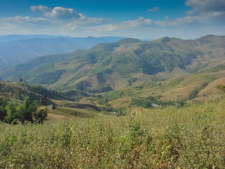 Fototapeta premium Mountain view of a small hut on top hill around with high mountains and blue sky background, Doi Chang, Chiang Rai, Thailand.