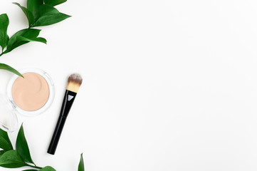 Face powder in round case and make up brush top view with green leaf background. Fashion cosmetic, natural makeup product composition. Open compact foundation cream. Organic facial concealer powder