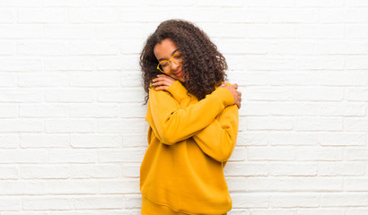 young black woman feeling in love, smiling, cuddling and hugging self, staying single, being selfish and egocentric against brick wall - obrazy, fototapety, plakaty
