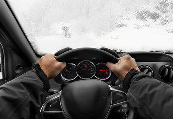 Driver holding steering wheel of a car with two hands and driving the car.