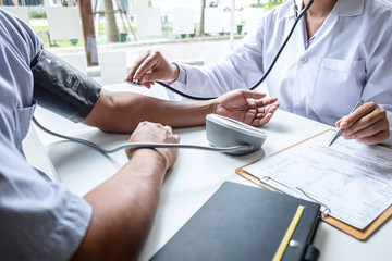 Doctor using stethoscope checking measuring arterial blood pressure on arm to a patient in the...