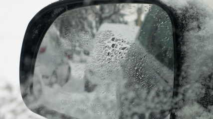 Close up - Looking in the rearview mirror. View of a cars stuck in the snow. Objects in the Mirror are Closer than They Appear.