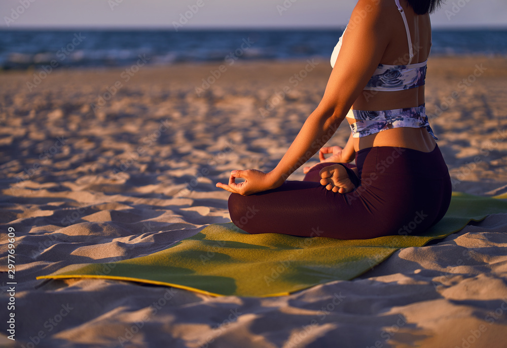 Wall mural young woman doing yoga by the sea