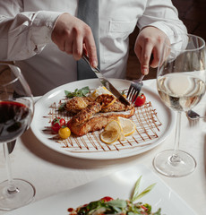 man cutting grilled salmon served with rice, lula kebab, lice, tomatoes, wine