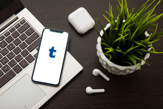 Tumblr logo on the iphone X screen is placed on the laptop keyboard next to AirPods.