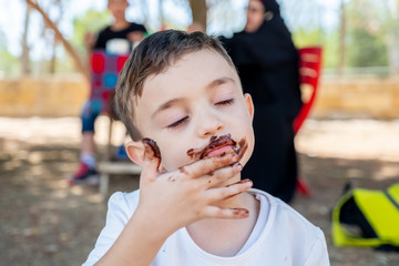 Happy little boy enjoying getting his hands covered with chocolate