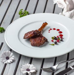 two pieces of lamb ribs kebab in white plate garnished with berry sauce