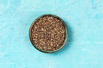 A bowl of chia seeds, shot from the top on a blue background with a place for text