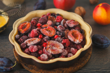 Homemade autumn red fruit pie, in a brown ceramic pie plate, ready to bake