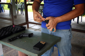 Blurry closeup a man hands holding and loading 9mm bullets in the pistol at the shooting range, is used for testing practice with paper target.
