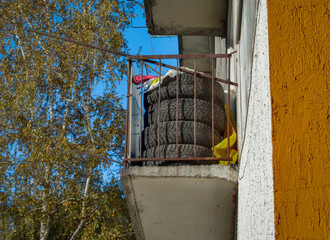 Used old car tires on balcony. Closeup. Blue sky. Residential building. Soviet architecture. Ust-kamenogorsk (Kazakhstan)