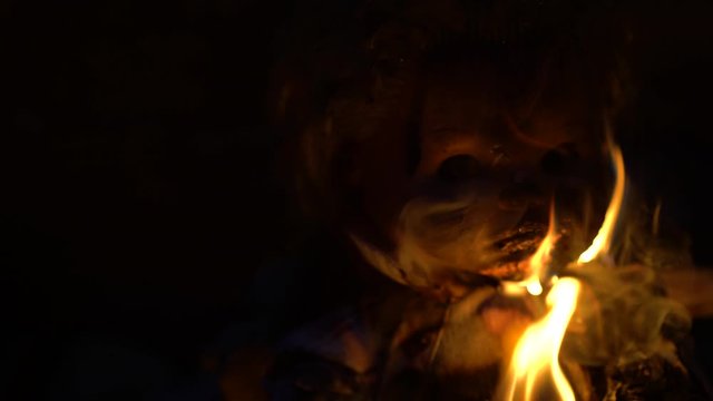 Close-up of devilish doll face burning on fire, occult ritual, black magic. Spooky Halloween scene