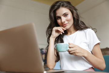 Happy young woman indoors at home using laptop