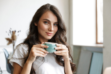 Happy young woman indoors at home drinking coffee.