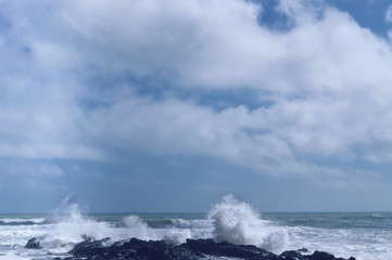 cloudscape over sea with waves hitting lava rock