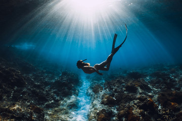 Attractive woman free diver glides with fins over sandy sea. Freediving in a tropical ocean