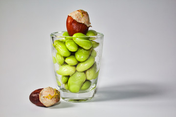 Green edamame beans in a small glass container on a white background