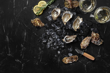Fresh opened oysters, ice, lemon on a rectangle slate and champagne are on a black stone textured...
