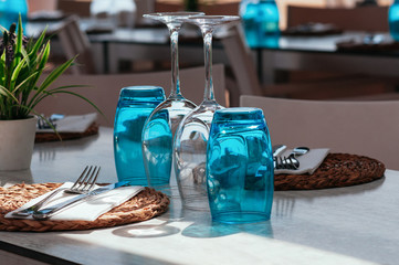 Table setup in restaurant on sunny day outdoor, served for lunch, blue glasses, wicker plates, cutlery. Simple, authentic decor. Beautiful summer holiday concept. Romantic time at resort