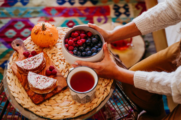 woman holding a bowl of fruits with blueberries and raspberries at home during breakfast. Cute golden retriever dog besides. Healthy breakfast with fruits and sweets. lifestyle indoors