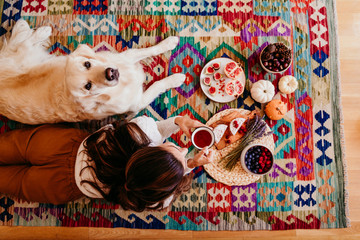 beautiful woman and cute golden retriever dog enjoying healthy breakfast at home, lying on the floor. healthy breakfast with tea, fruits and sweets. top view