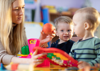 Children toddlers and nursery teacher play with toy scales in kindergarten playroom