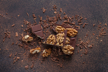 chocolate bar pieces with walnuts on brown background with chocolate crumbs. Top view
